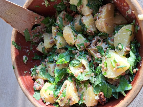 Miteinander vermengter Kartoffelsalat aus Knoblauchsrauke, Löwenzahn und Berglinsen in einer braunen Tonschüssel.
