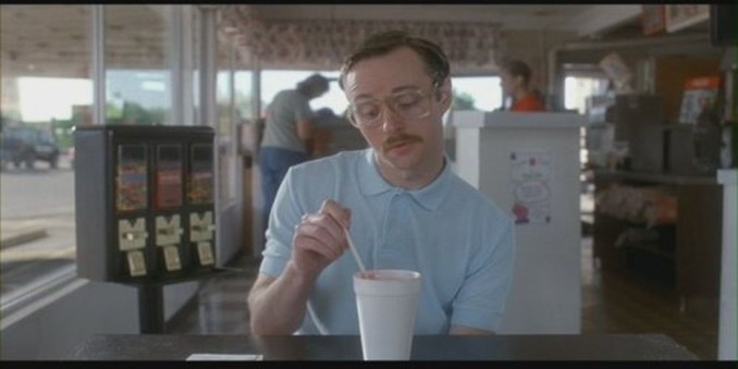 kip from Napoleon dynamite sitting in a diner looking down on his drink while stirring it.