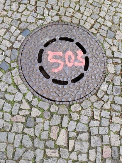 An iron manhole cover in a pavement, the number 503 sprayed with red paint on it.