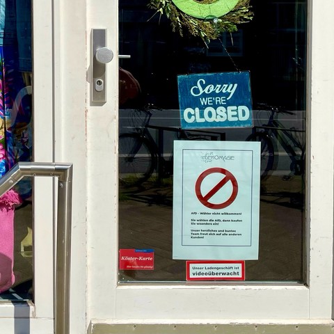 Ladentür (Dekomagie) mit einem „Sorry We're Closed“-Schild, einem Plakat mit einem Verbotssymbol und Text auf Deutsch sowie einem Hinweis auf Videoüberwachung.

Store door (Dekomagie) with a 