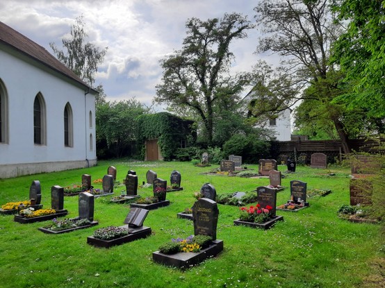Ein Grabfeld mit Urnengräbern. Gut angelegt mit ausreichend Platz zwischen den Reihen und Gräbern. Der Friedhof macht insgesamt einen gepflegten Eindruck. Links ein Teil der Kapelle.