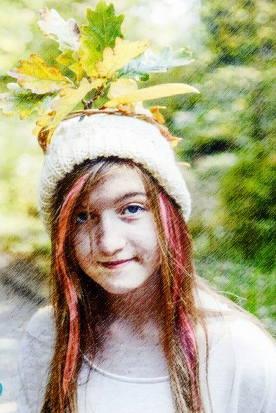 A young woman with long hair streaked with pink, who is smiling, and is wearing a knitted hat with a crown of leaves on top.