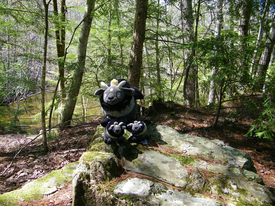 Three plush goats, one big and two small, standing on a rocky spot in a forest.
