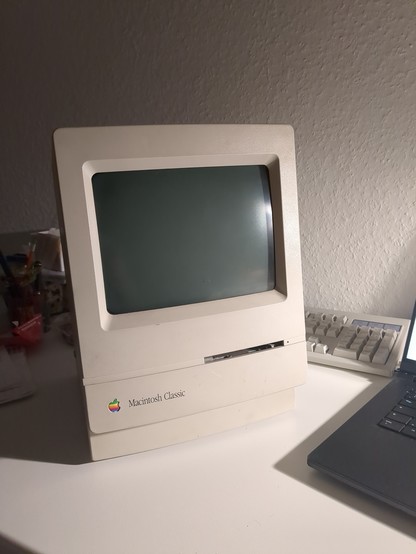 on a table sits, what looks like a beige CRT monitor with a lot of room underneath the screen where a slot for inserting floppy disks and a colorful apple logo with the label 