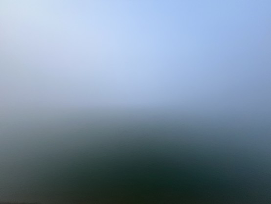A foggy, blurred landscape with a gradient transition from light blue at the top to dark green at the bottom.