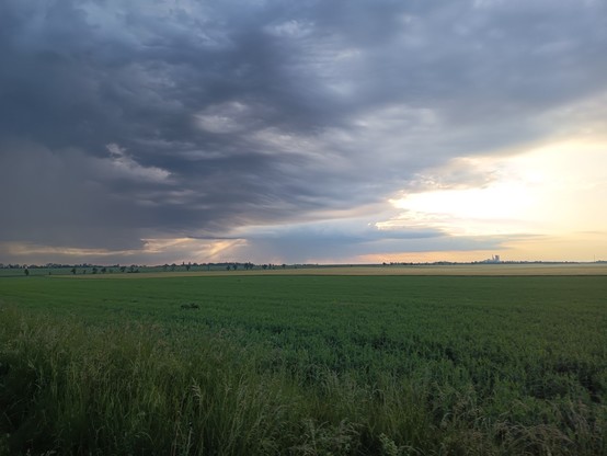Grey clouds in the left are pushed Back by the sunrise in the right side, over a field.