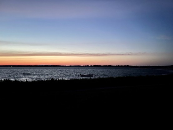 Ein ruhiger Sonnenuntergang über einem ruhigen Meer mit einem einsamen Boot am Horizont und einer Silhouette der Küstenlinie im Vordergrund.

A serene sunset over a calm sea with a lone boat on the horizon and a silhouette of the shoreline in the foreground.