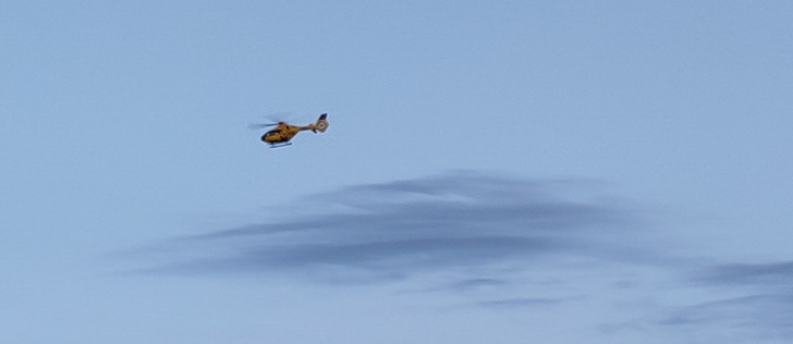 Ein ADAC Rettungshubschrauber fliegt vor einer Zirruswolke.