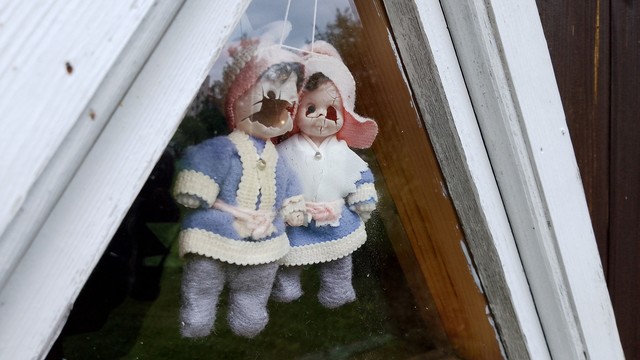 Two doll ornaments behind a small window. Cute couple destroyed by the UV exposure. Their faces cracked.