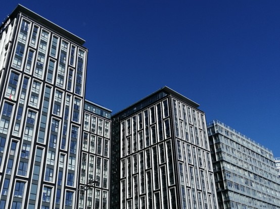 Mehrstöckige Gebäude, deren Fenster ganz viele Rechtecke bilden. Die Silhouette der Gebäude ergibt vor dem irgendwie sexy blauen Himmel eine Zickzack-Linie.