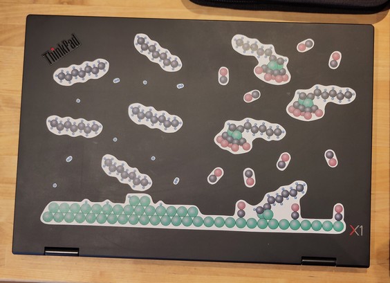 Ein Laptopdeckel mit vielen Stickern. Jeder Sticker zeigt bunte Moleküle. Vom Wasserstoff, über Kohlenmonoxid, Heptan bishin zu einem größeren Metallkomplex.