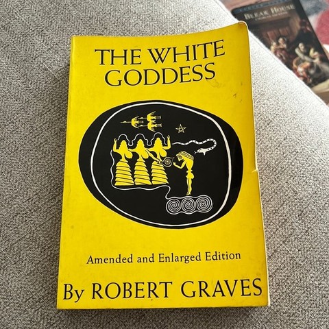 A book with a yellow cover. In the center is a circular shape in black, with drawings of three goddesses, and a male figure in yellow. There are also spirals and three flying geese, a snake and a pentagram.

The title type reads (in black letters):
THE WHITE GODDESS
Amended and Enlarged Edition
by ROBERT GRAVES