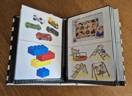 Mini-Fotoalbum als Kommunikationsbuch für ein non-verbales Kindergarten-Kind. Es gibt vier Bilder pro Seite, mit denen Wünsche und Bedürfnisse ausgedrückt werden können. Auf der aufgeschlagenen Seite sehen wir Spielzeug-Autos, Duplos, Memory und Spielplatz. 