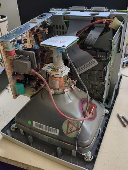 a photo showing the complex circuitry of the now naked computer. there's the back of the crt, different circuit board and a floppy drive.