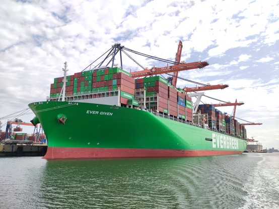 Ein riesiges grünes Containerschiff an einem Landehafen. Es sind tausende teils grüne Container auf dem Schiff. Auf dem Schiff steht evergreen und ever given.