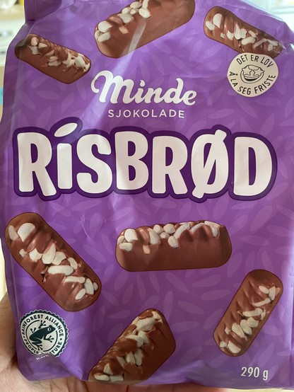 Packung einer norwegischen Süßigkeit „Risbrød“ welches kleine Schokoladenbarren mit Puffreis auf violettem Hintergrund zeigt.