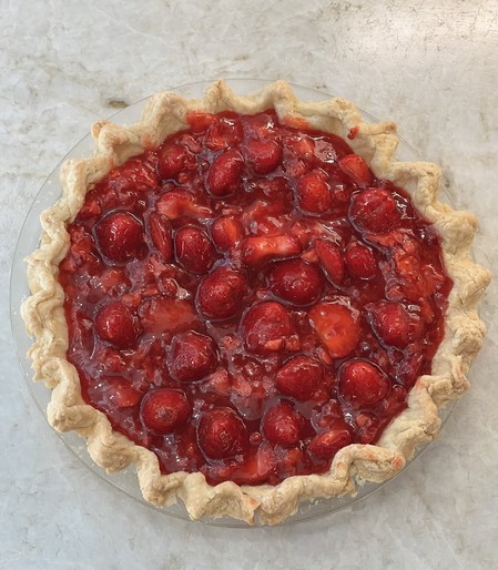 Bright red 9 inch strawberry pie with fluted edges on the crust, sitting on a stone counter 