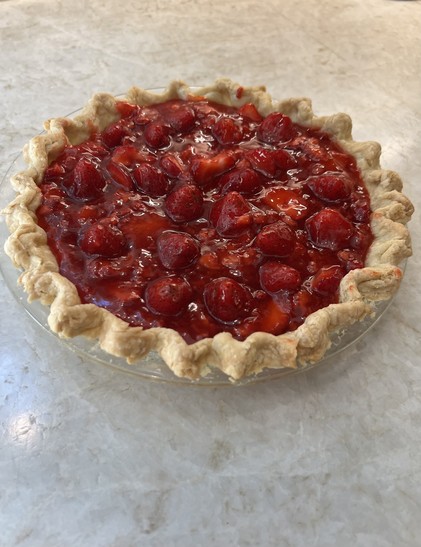 A strawberry pie with fluted crust in a stone counter