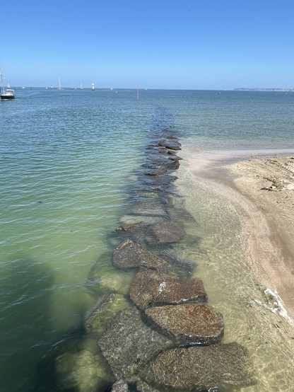 Große flache Steine im Wasser entlang einer Hafenausfahrt sehen aus wie ein Weg für Riesen. Das Wasser ist grün-blau, der Himmel blau. Diesen „Weg“ darf man nicht begehen wegen Lebensgefahr.