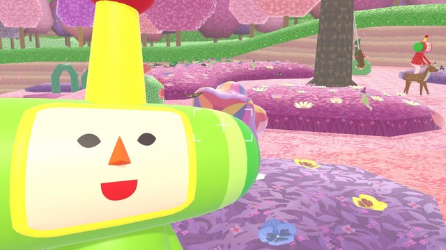 Aus dem Spiel We love Katamari. In einer fantastischen, lilafarbenen Waldlandschaft steht eine merkwürdige, grüne Figur, die fröhlich lächelt und ein Selfie macht. Ihr zylinderförmiger Kopf ist quer auf dem Körper positioniert, was ihr ein einzigartiges und skurriles Aussehen verleiht. Die lebendige Ausstrahlung und die ungewöhnliche Umgebung verleihen der Szene einen spielerischen und farbenfrohen Charakter. Die Kombination aus der leuchtend grünen Figur und dem lila Wald schafft ein faszinierendes und surrealistisches Bild, das die verspielte Atmosphäre des Spiels Katamari perfekt einfängt