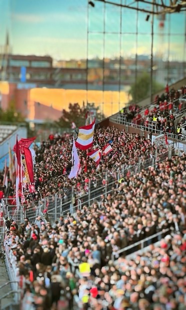 Eine große Menge von Fans versammelte sich in einem Stadion, viele mit bunten Fahnen. Die Szene fängt die lebendige Atmosphäre eines Sportereignisses ein, mit Tribünen voller begeisterter Zuschauer.

A large crowd of fans gathered in a stadium, many holding colorful flags. The scene captures the vibrant atmosphere of a sporting event, with stands filled with enthusiastic spectators.