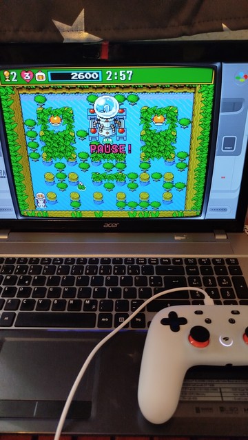 Ein Bild von meinem Laptop auf dem ein weißer Controller liegt. Darauf Läuft Bomberman 3 vom SNES, ein Topdown Spiel das in diesem Bild aus vielen Bäumen besteht und nur schmale gänge dem Spieler Platz geben