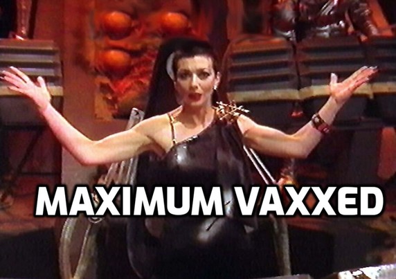 Servalan, standing on the bridge of the Liberator, arms flung dramatically wide. Caption: Maximum vaxxed.