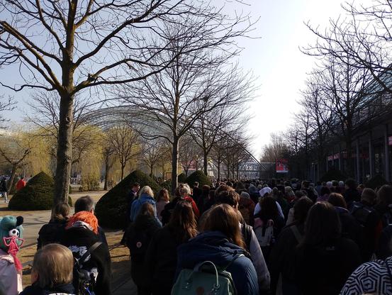 Menschenmenge bewegt sich auf die Glashalle der Messe zu